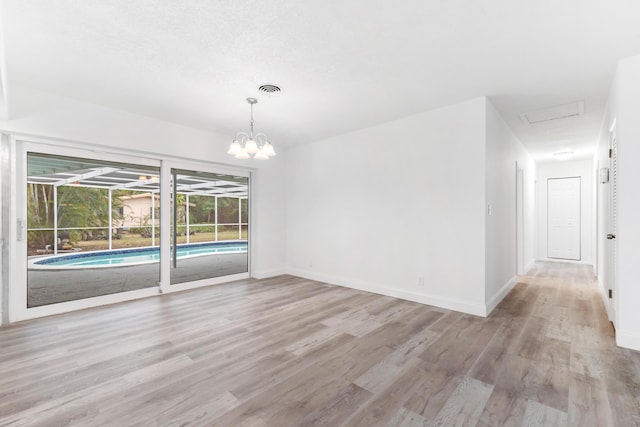 empty room featuring baseboards, visible vents, light wood-style flooring, and a notable chandelier