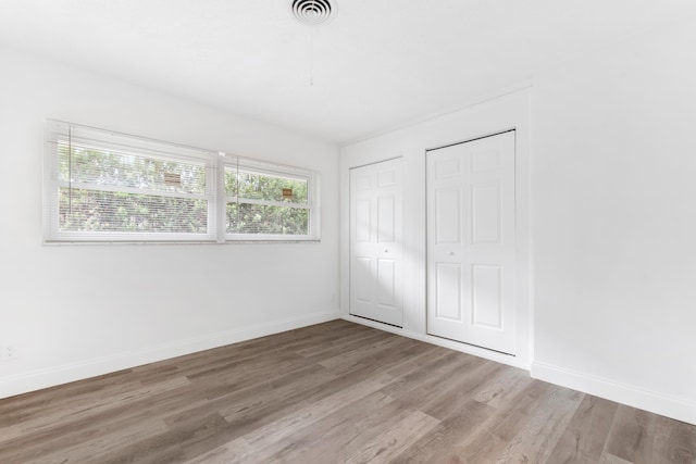 unfurnished bedroom with baseboards, visible vents, wood finished floors, and multiple closets