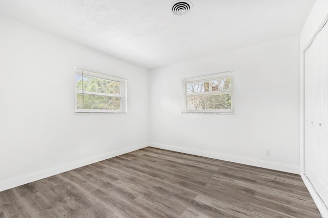 spare room featuring baseboards, visible vents, a textured ceiling, and wood finished floors