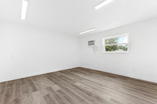 unfurnished room featuring baseboards, a wall unit AC, and wood finished floors