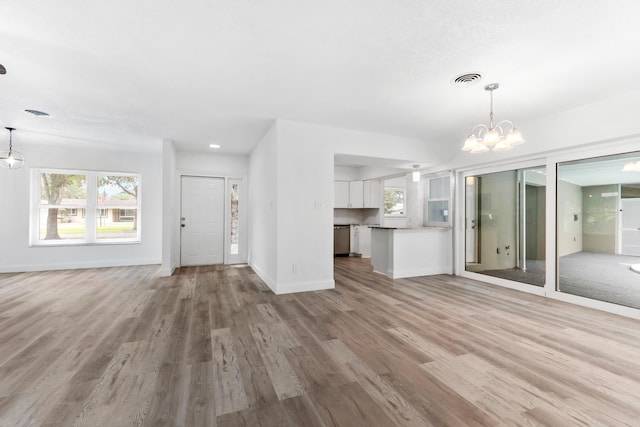 unfurnished living room with visible vents, wood finished floors, a notable chandelier, and plenty of natural light