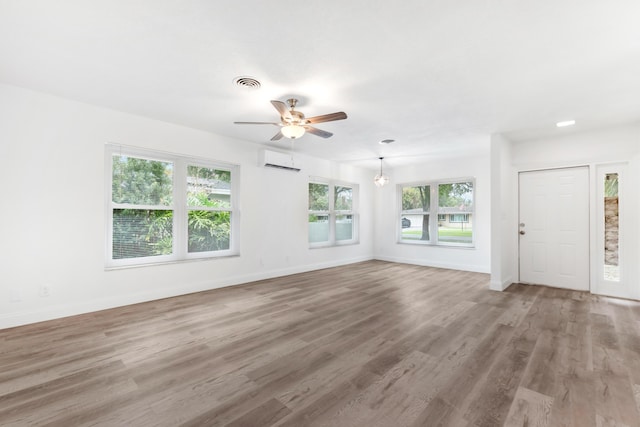 unfurnished living room featuring a ceiling fan, light wood-type flooring, baseboards, visible vents, and an AC wall unit
