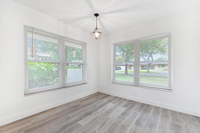 empty room featuring baseboards, light wood-type flooring, and an inviting chandelier