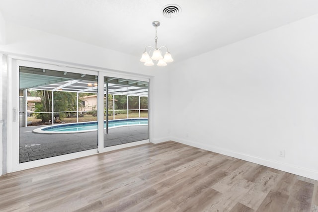 empty room with baseboards, visible vents, a notable chandelier, and wood finished floors