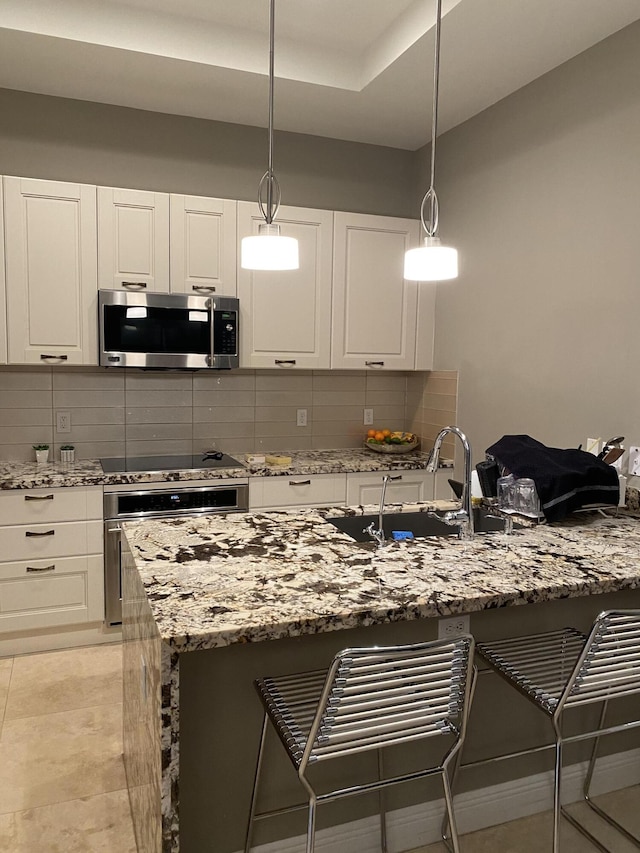 8481 NW 51st Ter, Doral, FL 33166 - kitchen featuring light stone counters, white cabinetry, a breakfast bar area, stainless steel appliances, and decorative backsplash