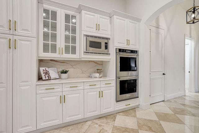9387 Satinleaf Pl, Parkland, FL 33076 - kitchen with white cabinetry, backsplash, light countertops, arched walkways, and appliances with stainless steel finishes
