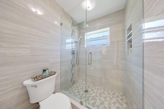 bathroom featuring toilet, a stall shower, and tile walls