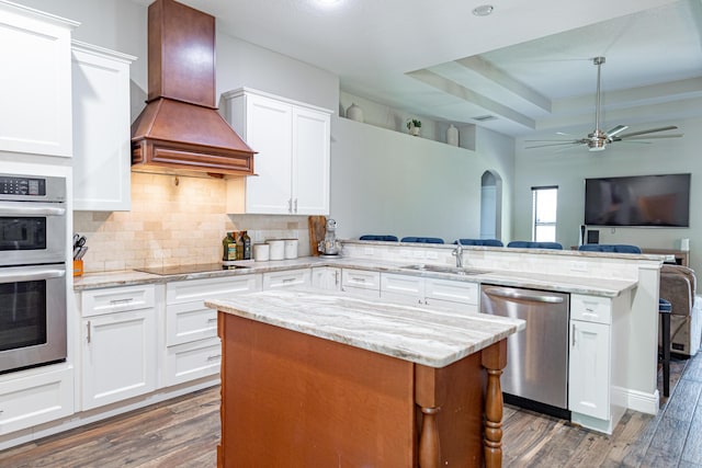 kitchen featuring a peninsula, stainless steel appliances, open floor plan, premium range hood, and dark wood-style floors