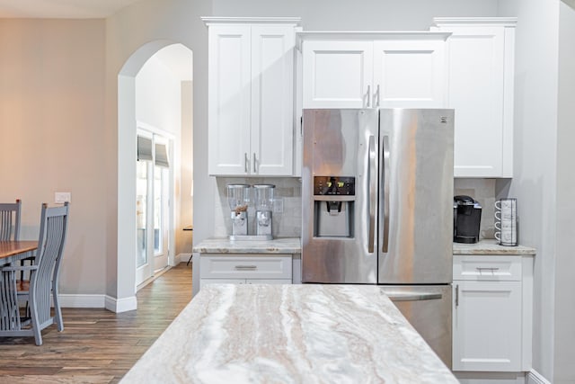 kitchen featuring stainless steel fridge with ice dispenser, arched walkways, wood finished floors, baseboards, and backsplash