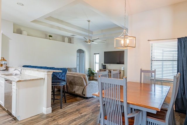 dining room featuring arched walkways, a tray ceiling, a ceiling fan, and wood finished floors