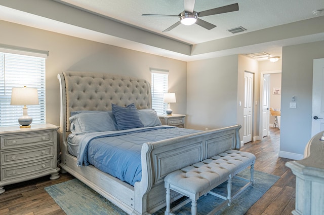 bedroom featuring a tray ceiling, visible vents, dark wood-style flooring, and baseboards