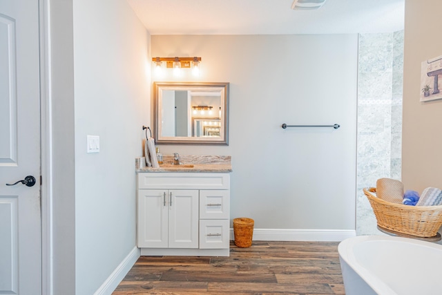 bathroom featuring baseboards, a soaking tub, wood finished floors, and vanity