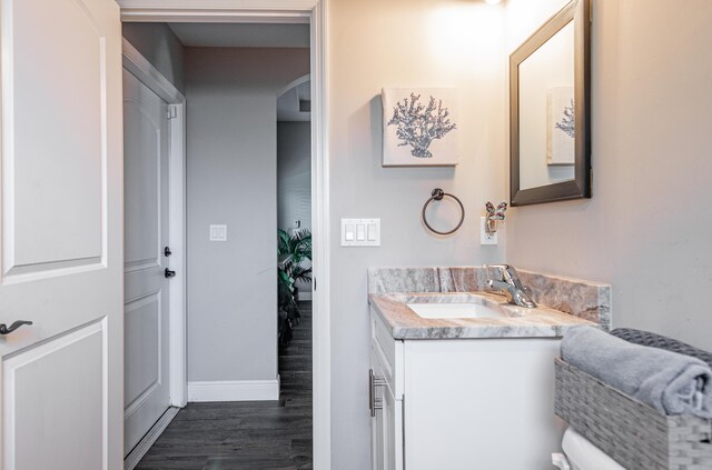 half bath featuring vanity, baseboards, and wood finished floors