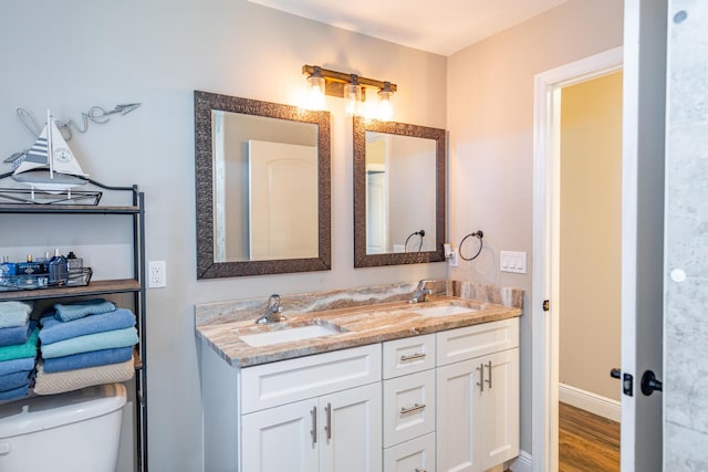 bathroom with double vanity, a sink, toilet, and wood finished floors