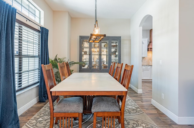 dining area featuring arched walkways, wood finished floors, and baseboards