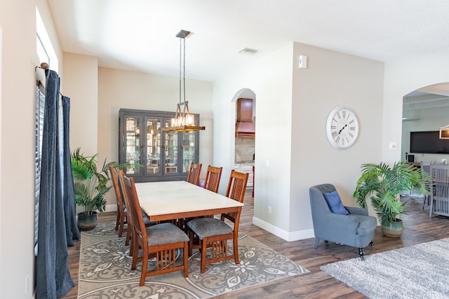 dining space with a chandelier, arched walkways, baseboards, and wood finished floors