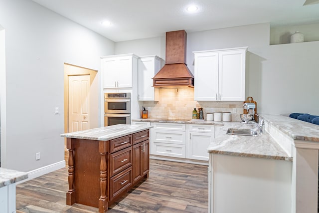 kitchen featuring double oven, a peninsula, custom exhaust hood, a sink, and dark wood-style floors