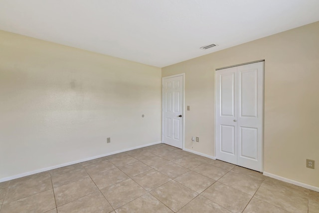 unfurnished bedroom featuring baseboards, a closet, visible vents, and light tile patterned floors