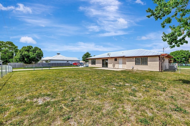 rear view of property with a patio area, a fenced backyard, a yard, and metal roof