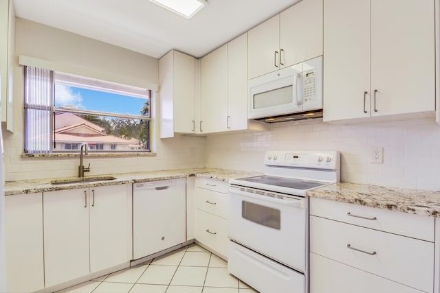 kitchen featuring light stone countertops, a sink, white appliances, decorative backsplash, and light tile patterned floors