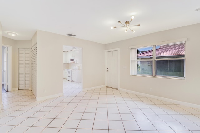 empty room with baseboards, a chandelier, light tile patterned floors, and visible vents