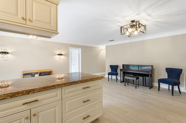 kitchen featuring light wood-style flooring, cream cabinetry, baseboards, and dark stone counters