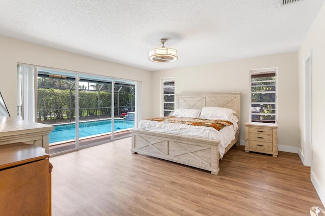 bedroom with multiple windows, access to outside, wood finished floors, and a textured ceiling