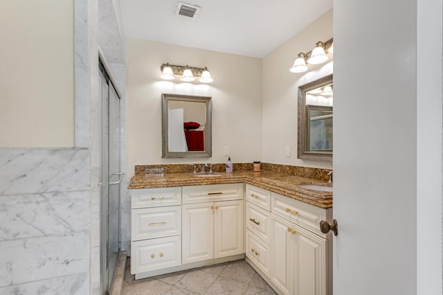 bathroom with a stall shower, double vanity, a sink, and visible vents