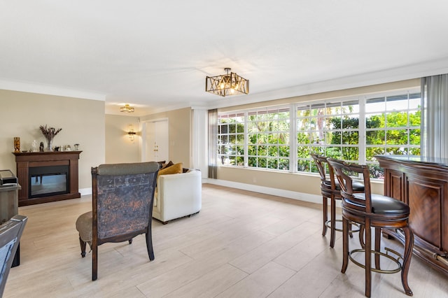 living area with a glass covered fireplace, a notable chandelier, baseboards, crown molding, and light wood finished floors