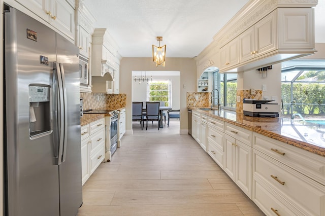 kitchen featuring light stone counters, a chandelier, backsplash, appliances with stainless steel finishes, and a sink