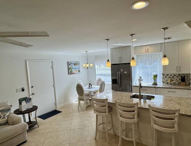 kitchen featuring decorative backsplash, light tile patterned flooring, a sink, light stone counters, and stainless steel fridge with ice dispenser