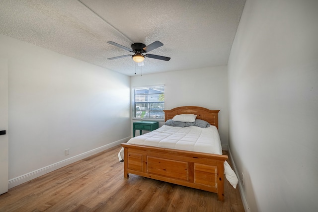 bedroom featuring baseboards, ceiling fan, a textured ceiling, and wood finished floors