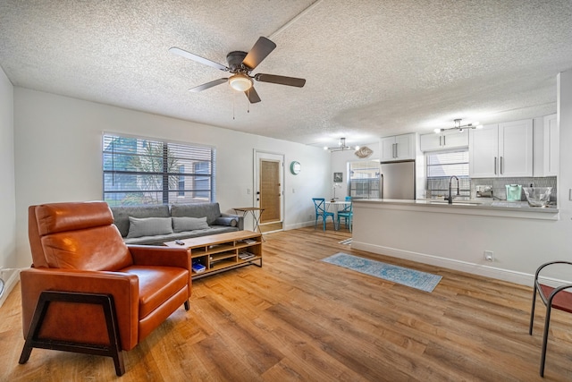 living area featuring light wood-type flooring, a textured ceiling, and ceiling fan with notable chandelier