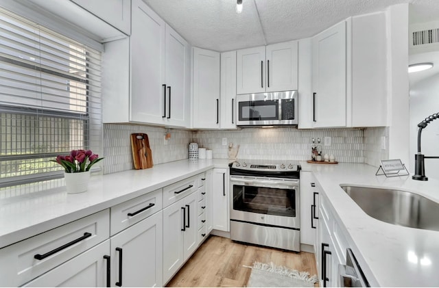 kitchen with stainless steel appliances, visible vents, white cabinetry, and a sink