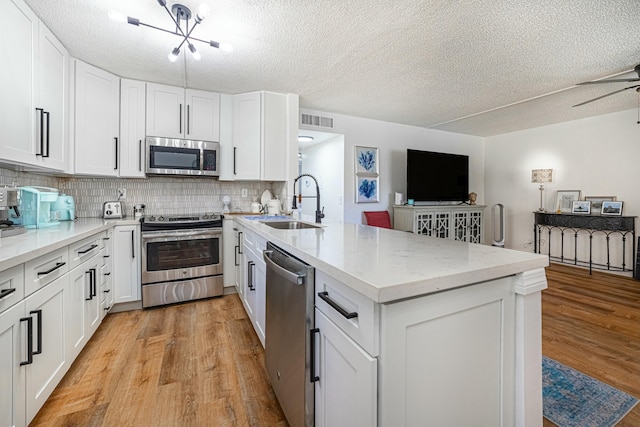 kitchen with a sink, light wood-style flooring, stainless steel appliances, a peninsula, and visible vents
