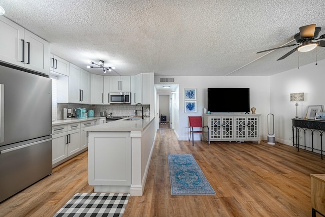 kitchen with visible vents, a sink, light countertops, a peninsula, and stainless steel appliances