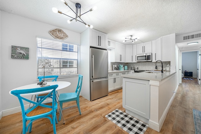 kitchen with light countertops, a textured ceiling, a sink, appliances with stainless steel finishes, and a notable chandelier