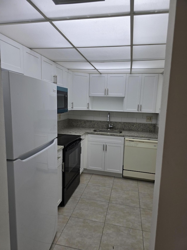 kitchen featuring light tile patterned flooring, a sink, dark stone countertops, white cabinetry, and black appliances