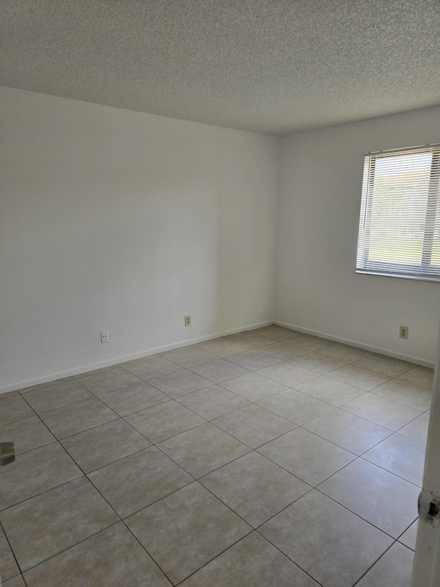unfurnished room with light tile patterned floors, baseboards, and a textured ceiling