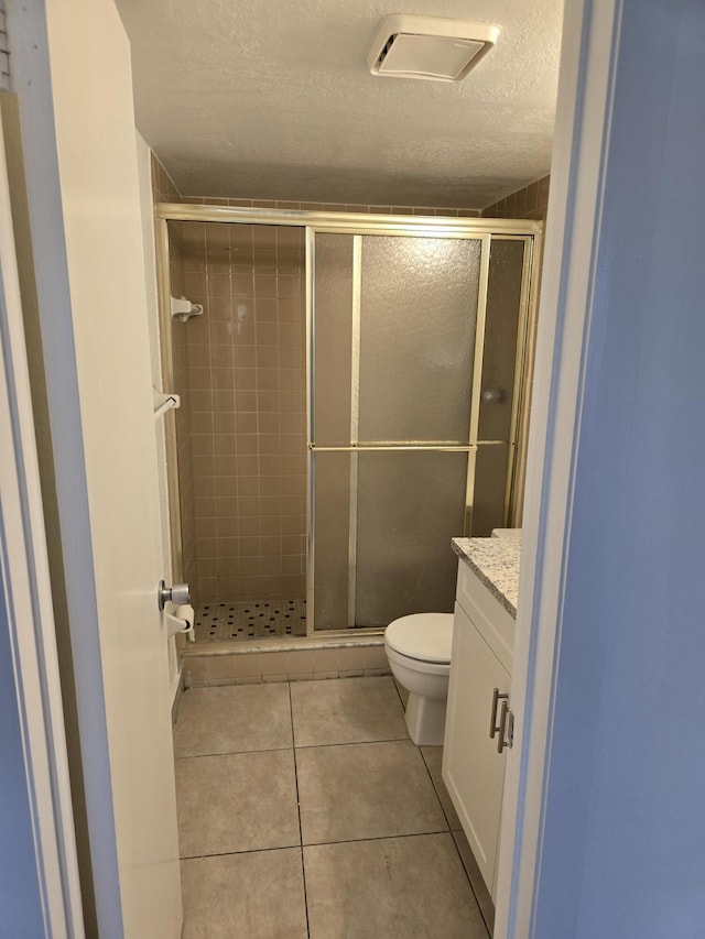 full bathroom featuring tile patterned flooring, a textured ceiling, a stall shower, and toilet