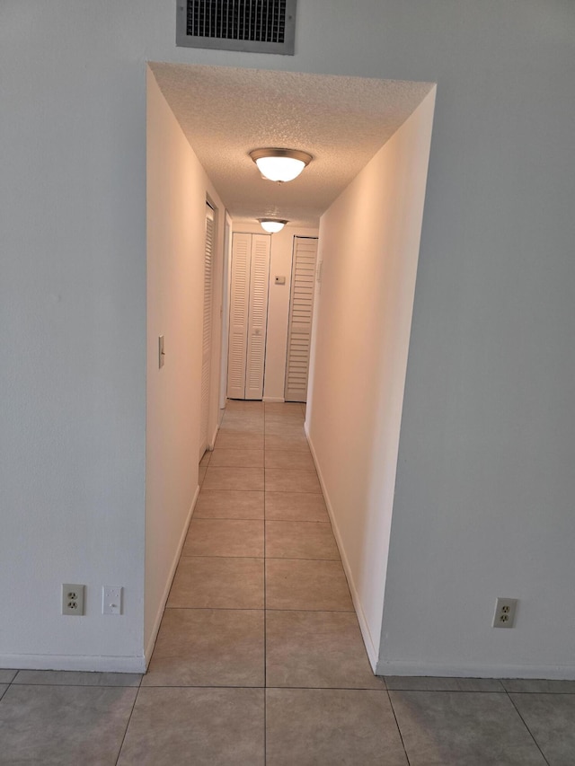 hall featuring a textured ceiling, baseboards, visible vents, and light tile patterned floors