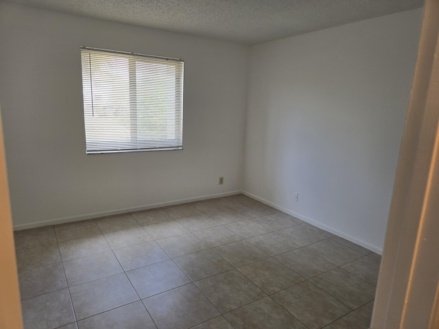 spare room featuring tile patterned flooring, a textured ceiling, and baseboards