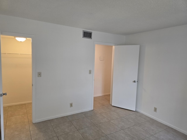 tiled spare room with visible vents, a textured ceiling, and baseboards