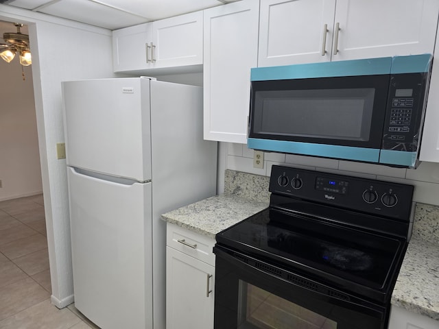 kitchen with black / electric stove, light stone countertops, light tile patterned floors, freestanding refrigerator, and white cabinetry
