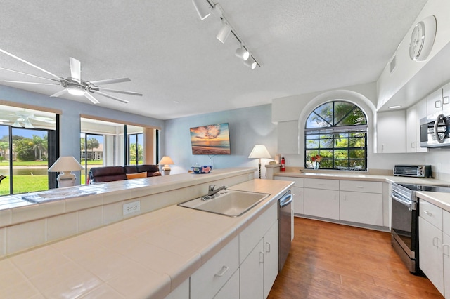 kitchen featuring tile counters, plenty of natural light, stainless steel appliances, a sink, and light wood finished floors