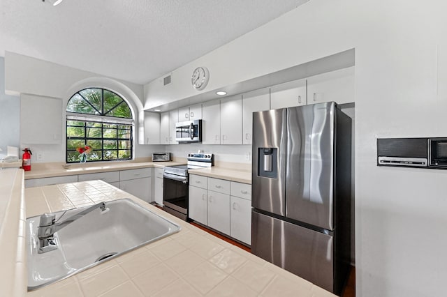 kitchen featuring a sink, white cabinetry, a textured ceiling, stainless steel appliances, and visible vents