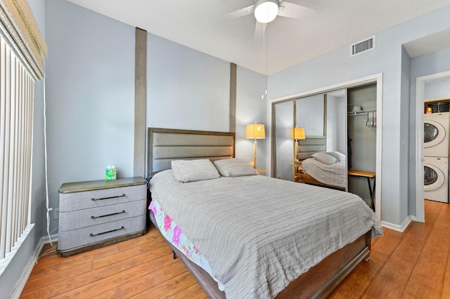bedroom with a closet, visible vents, stacked washer and clothes dryer, baseboards, and light wood-style floors