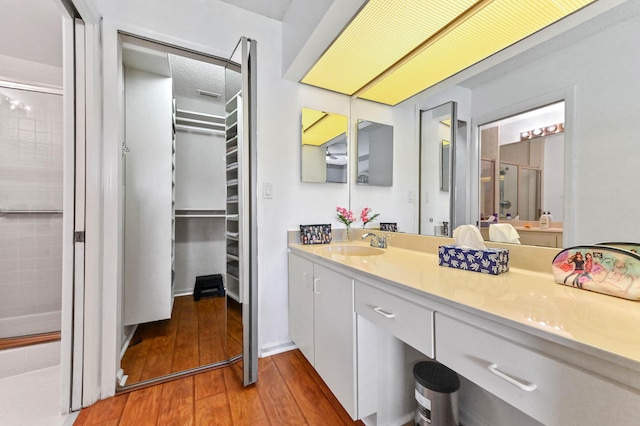 bathroom with vanity, wood finished floors, a spacious closet, and a shower stall