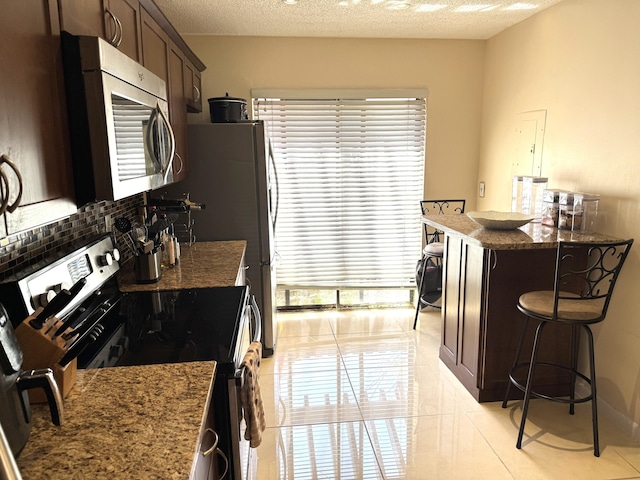3779 Carambola Cir N Unit 28102, Coconut Creek, FL 33066 - kitchen featuring appliances with stainless steel finishes, a breakfast bar, dark brown cabinetry, decorative backsplash, and healthy amount of natural light