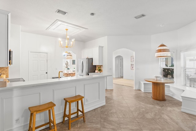 kitchen featuring freestanding refrigerator, arched walkways, light countertops, a peninsula, and hanging light fixtures